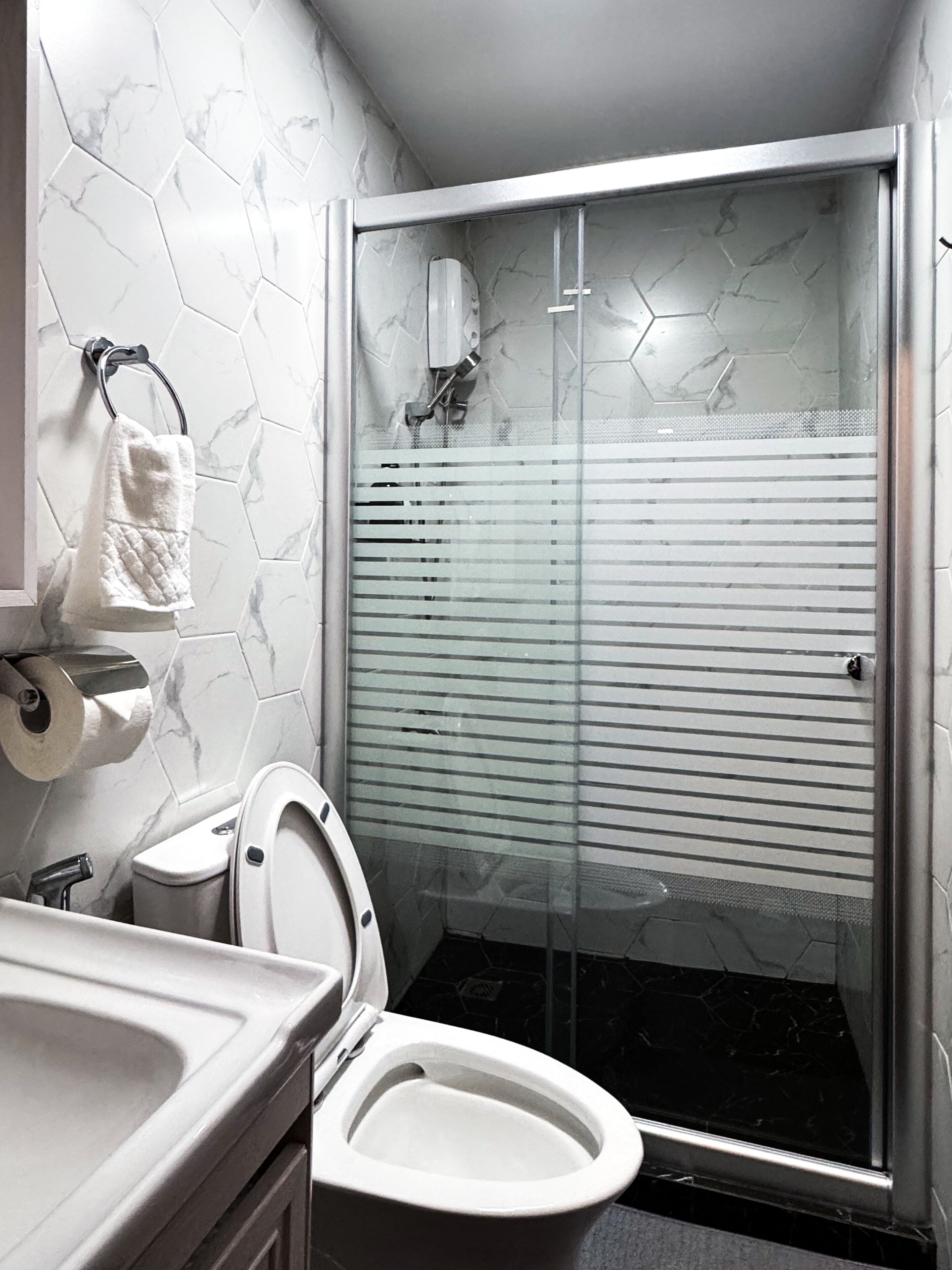 A modern bathroom with a white toilet, a glass-enclosed shower, and a marble-patterned wall.