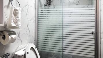 A modern bathroom with a white toilet, a glass-enclosed shower, and a marble-patterned wall.