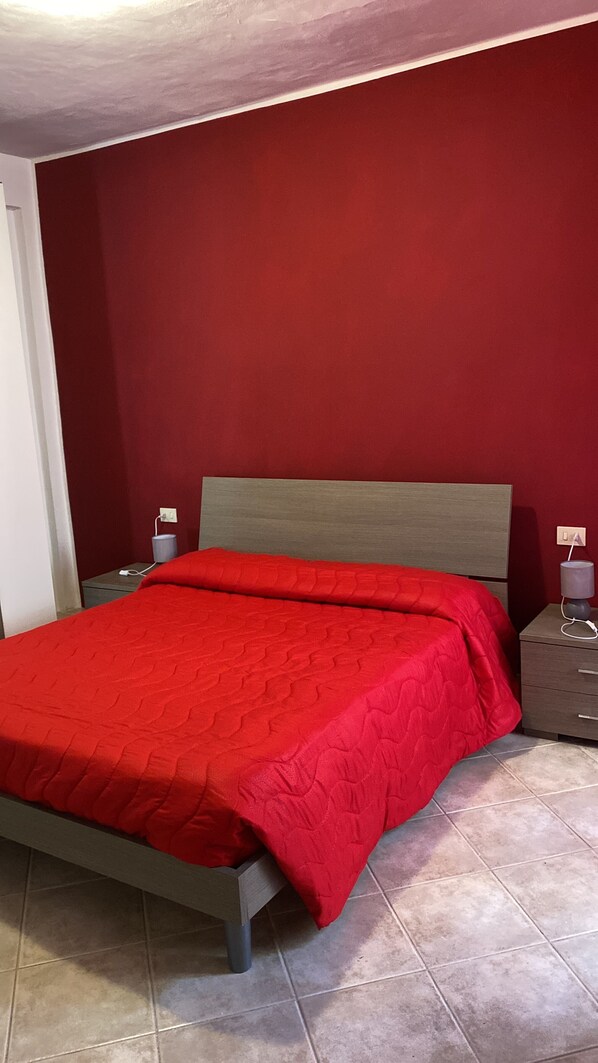 Una camera da letto con un letto, un comodino, una lampada e una parete rossa.