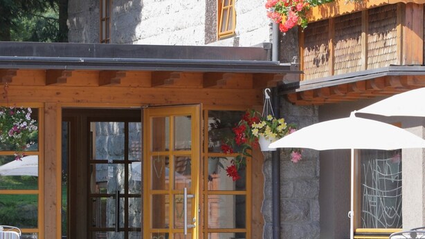 A wooden building with a stone facade, a wooden door, and hanging flower baskets.