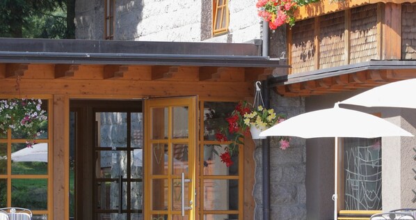 Un bâtiment en bois avec une façade en pierre, une porte en bois et des jardinières suspendues.