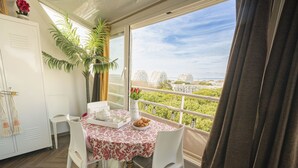 Ein Balkon mit Esstisch, gedecktem Frühstücksteller, einer Topfpflanze und Blick auf Gebäude.