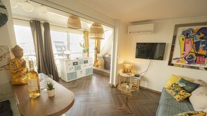 Ein modernes Wohnzimmer mit Holzboden, einer Couch mit bunten Kissen, einem Glastisch, einem weißen Schrank und einer Buddha-Statue.