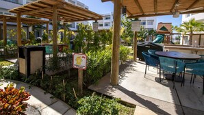 Un espacio al aire libre con un patio amueblado, pérgolas de madera y un cartel que indica un contenedor de reciclaje.