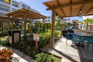 An outdoor patio area with wooden pergolas, seating arrangements, and a sign indicating a recycling bin.