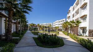 A hotel courtyard with a central garden, palm trees, and a pathway leading to the building.