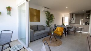 A modern living room with a grey sofa, a yellow armchair, and a dining area with a kitchen in the background.