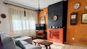Een woonkamer met een bank, een televisie, een open haard en een wandklok.