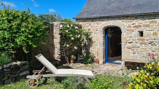 A stone building with a blue door, a garden with various plants, and a wooden chair. - Quiet house with private garden close to the sea (Roscoff)