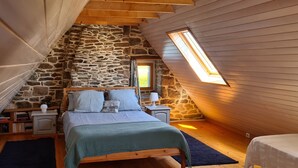 A cozy attic bedroom with a stone wall, a sloped ceiling, a skylight, a bed with pillows, a nightstand, and a lamp. - Quiet house with private garden close to the sea (Roscoff)
