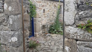 A stone building with a blue door, a small garden area with plants, and a stone pathway leading to the entrance. - Quiet house with private garden close to the sea (Roscoff)