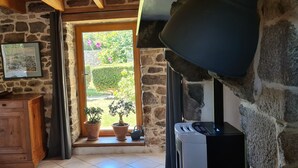 A stone-walled room with a wooden cabinet, a heater, and a window with a view of a garden. - Quiet house with private garden close to the sea (Roscoff)