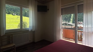 Quarto com uma cama grande, um radiador, uma cadeira e uma varanda com vista para uma paisagem verde.
