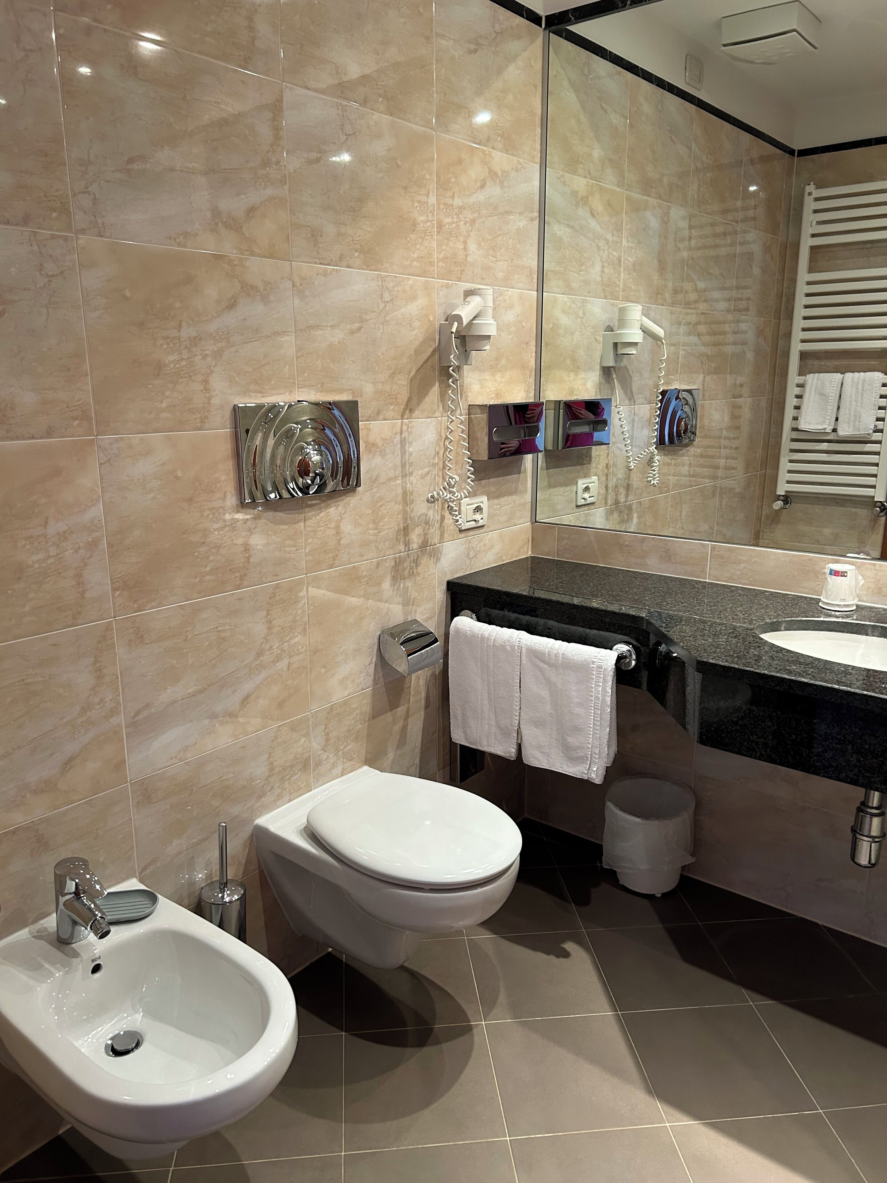 A modern bathroom with a bidet, toilet, sink, and a large mirror.