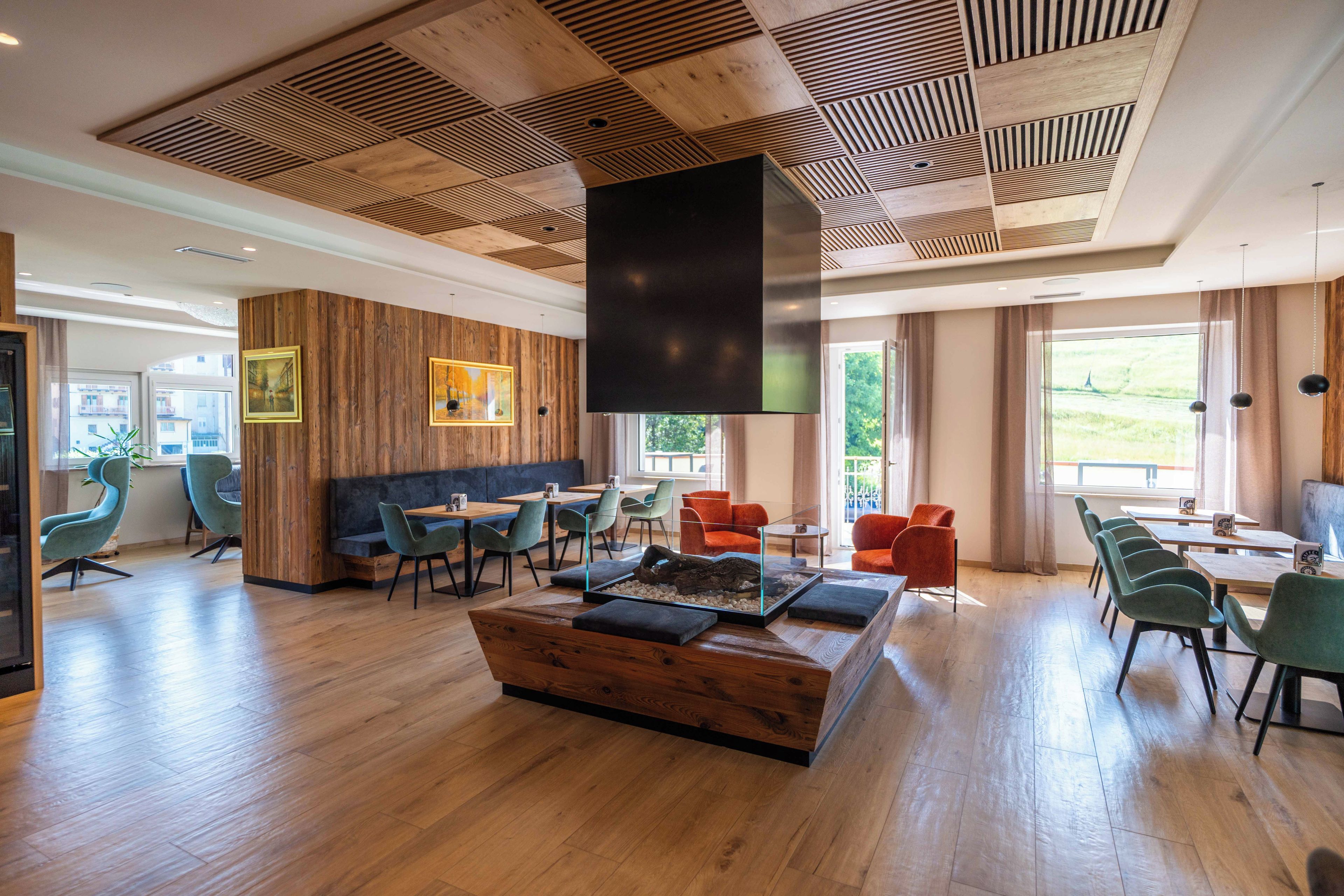 Ein modernes Interieur mit holzverkleideten Wänden, einer zentralen Sitzecke mit Tischen und Stühlen sowie großen Fenstern, die für natürliches Licht sorgen.