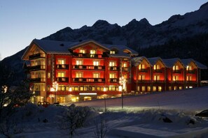 Un hotel grande de varios pisos con fachada roja y balcones, rodeado de montañas nevadas.