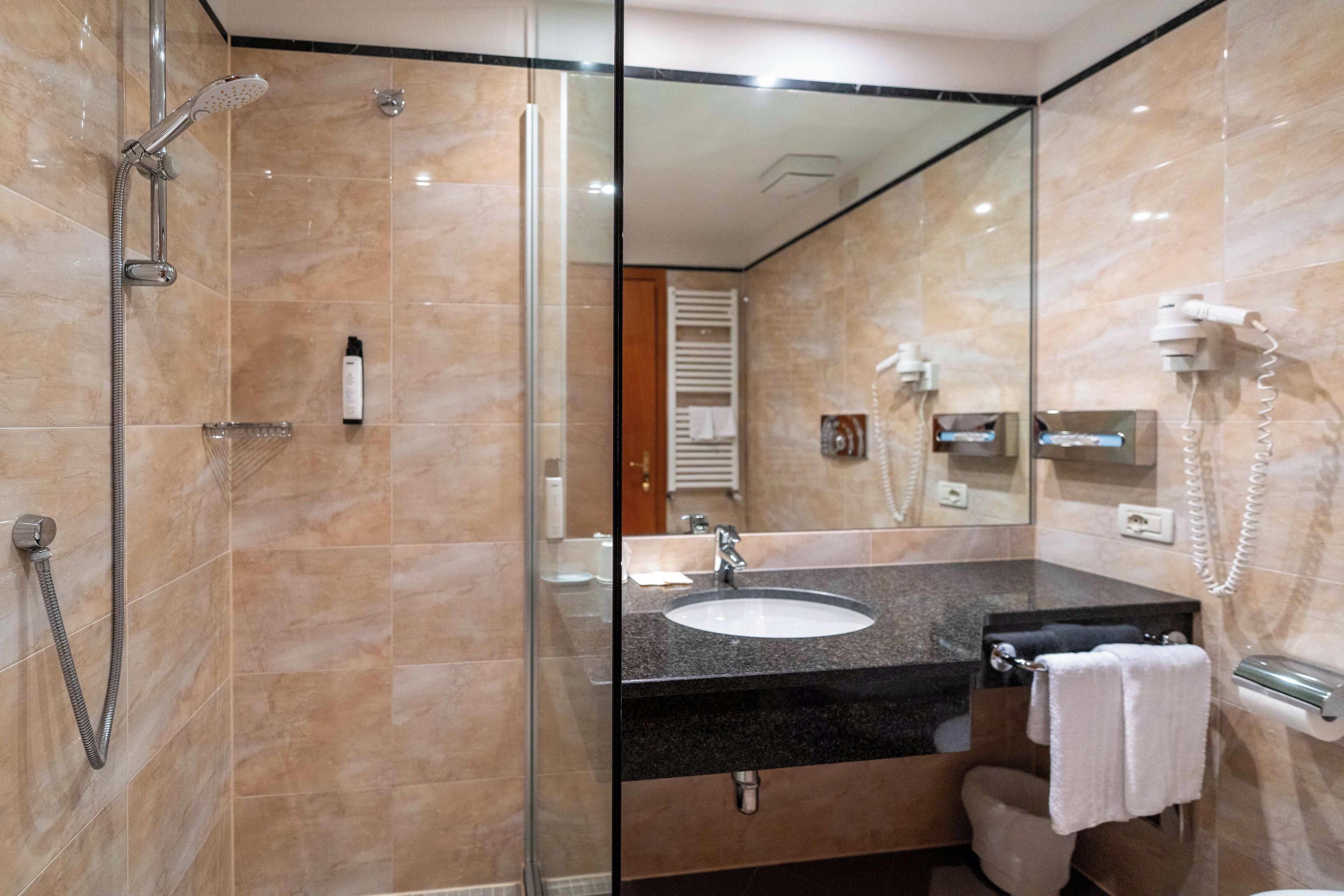 A modern bathroom with a glass shower enclosure, a sink with a black countertop, and a mirror reflecting the room.