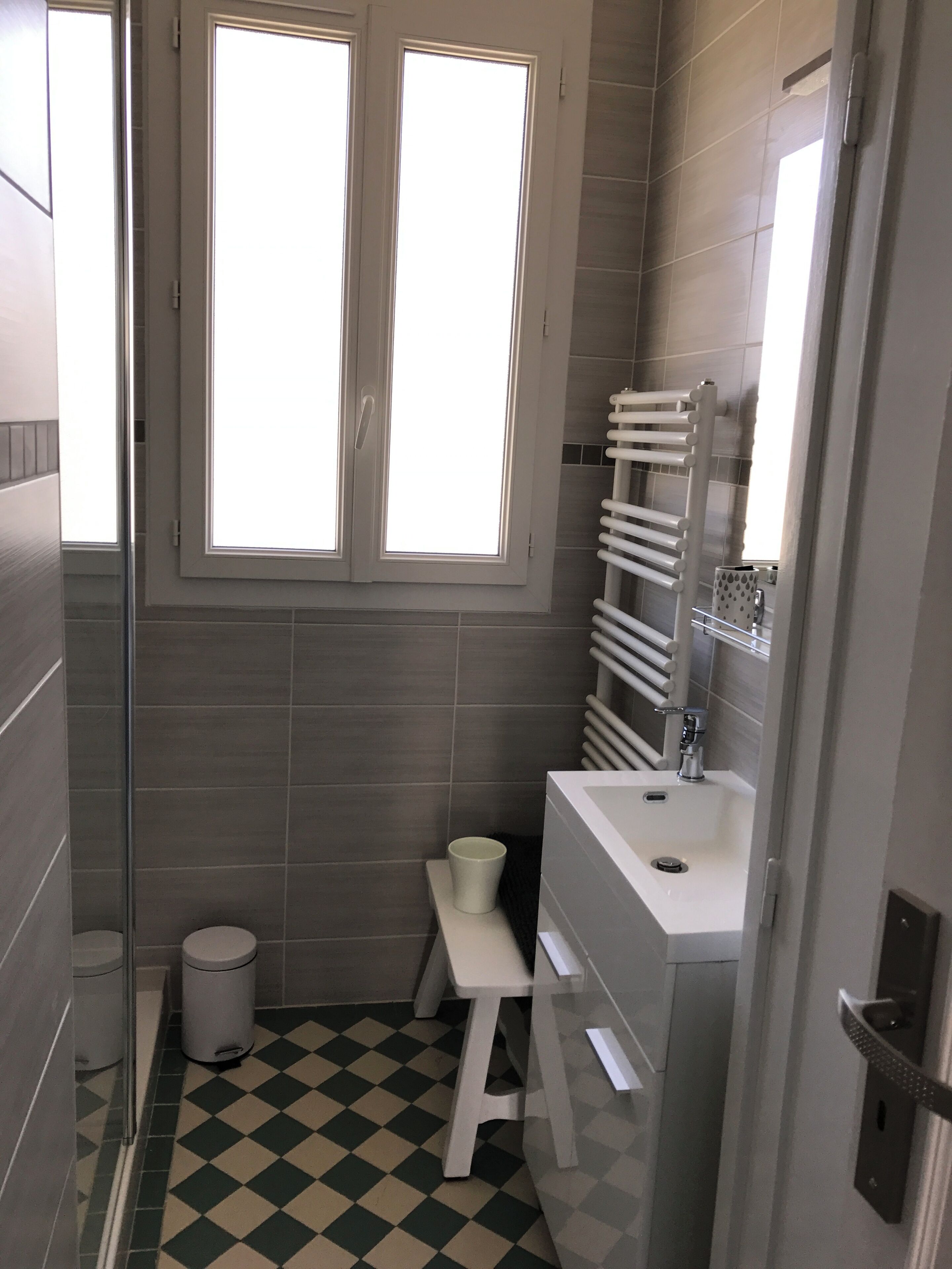 Une petite salle de bain moderne avec un carrelage à motifs, un lavabo blanc, des toilettes et une fenêtre située au-dessus du miroir.
