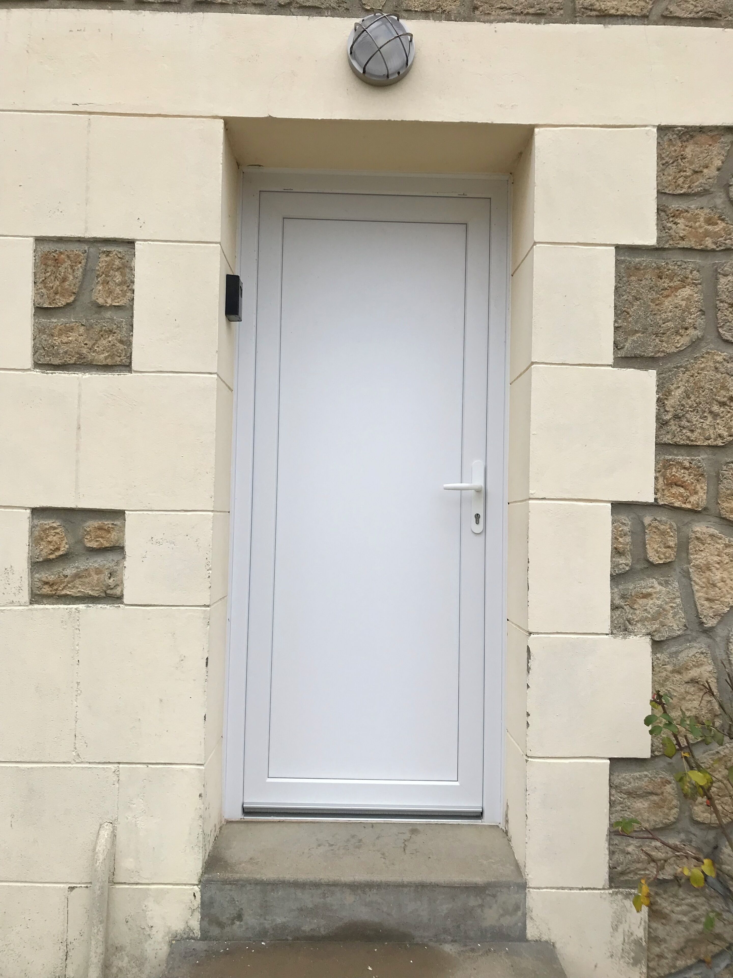 A white door with a keyhole, set in a stone and plaster wall with a small window above.