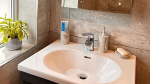 Une salle de bain avec un lavabo blanc, un miroir et une plante en pot.