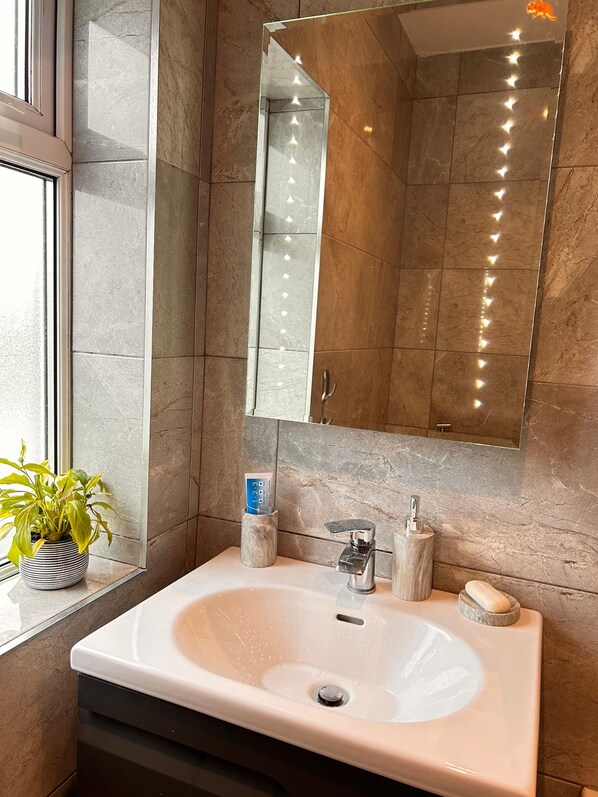 Un baño con lavamanos blanco, espejo y planta en maceta.