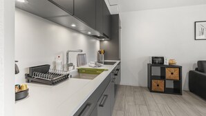 Une cuisine moderne avec un plan de travail blanc, des meubles gris et un meuble de rangement noir agrémenté de paniers en osier.