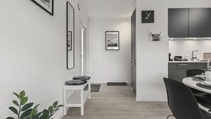Une cuisine moderne avec des meubles de couleur sombre, un coin repas avec une table blanche et des chaises noires, et un couloir orné de tableaux encadrés.