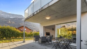 Une terrasse extérieure moderne, dotée d’un espace repas, d’un téléviseur et offrant une vue sur les montagnes.