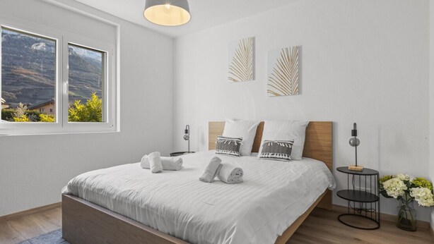 Une chambre moderne avec un grand lit, un luminaire suspendu et deux œuvres d’art accrochées au mur.