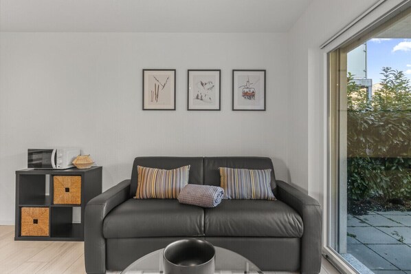 A modern living room with a grey sofa, two striped pillows, a small side table with a microwave, and three framed artworks on the wall.