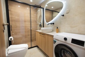 A modern bathroom with a toilet, sink, and washing machine. - Amazing Villa Eualia w pool (Hersonissos)