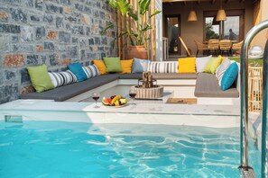A poolside area with a stone wall, a seating area with cushions, and a fruit bowl with drinks. - Amazing Villa Eualia w pool (Hersonissos)
