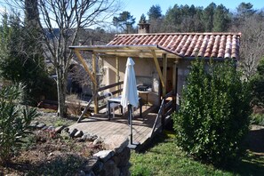 Une structure rustique en bois, avec un toit en tuiles, une table entourée de chaises et un mur en pierre.
