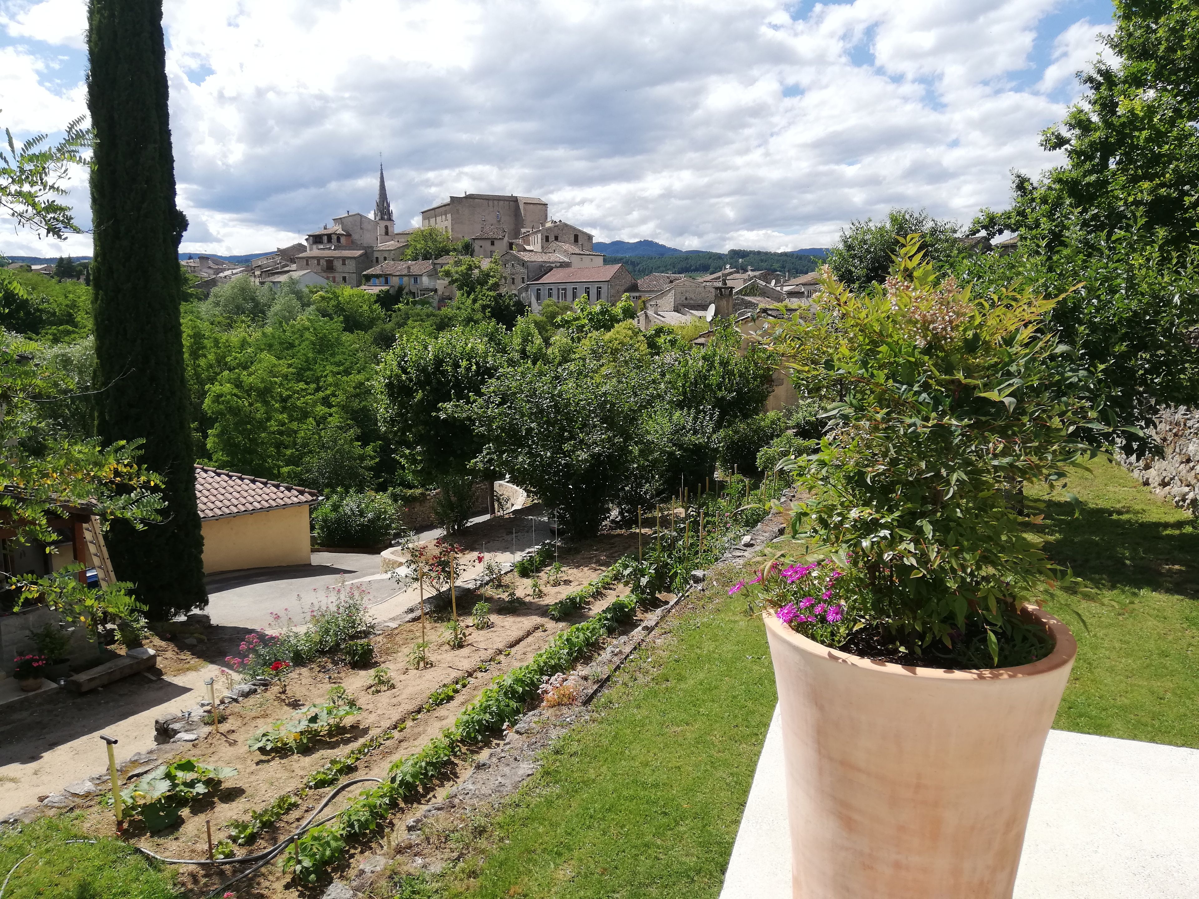 Un jardin où l’on trouve une grande variété de plantes, et d’où l’on peut admirer un village aux bâtiments traditionnels.