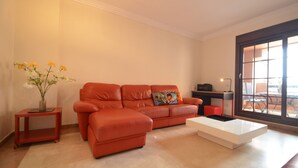 A living room with a red leather sofa, a white coffee table, and a small side table with a vase of flowers. - PLAYA VERDE 37 - Two Bedroom Apartment, Sleeps 5 (Punta del moral)