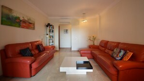 A living room with two red leather sofas, a white coffee table, a bookshelf, and a painting on the wall. - PLAYA VERDE 37 - Two Bedroom Apartment, Sleeps 5 (Punta del moral)