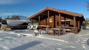 A log cabin with a covered porch, outdoor seating, and a snow-covered environment. - Fjordhygge (Jægerspris)