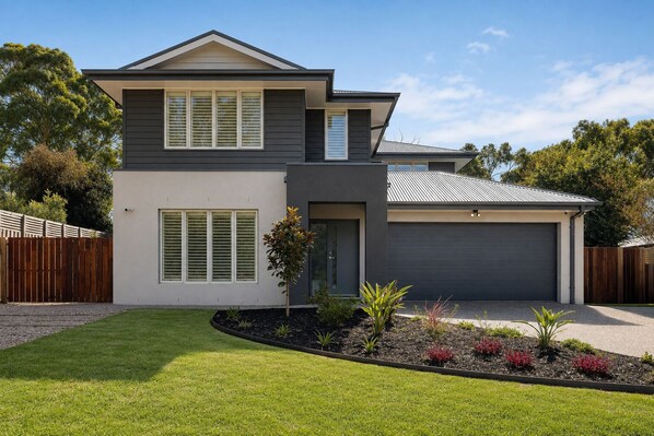 A modern two-story house with a garage, a well-maintained lawn, and a wooden fence.