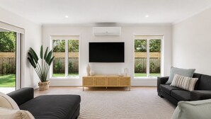 Uma sala de estar moderna com uma televisão de tela plana grande, um console de madeira e um sofá de couro preto.