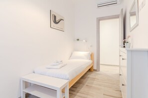 A minimalist bedroom with a single bed, a bedside table, a nightstand, a dresser, and a door leading to another room. - Maria Magdalena Apartment Saint Peter's (Roma)