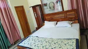 Une chambre à coucher avec un lit en bois, du linge de lit blanc, un plaid à motifs floraux, une armoire en bois et un meuble vitré contenant des objets décoratifs.