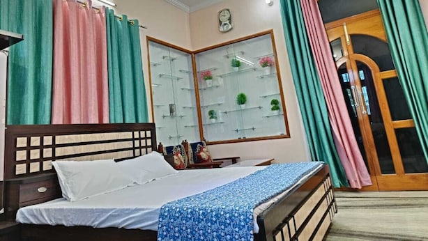 Une chambre à coucher avec un lit, une table de chevet, un miroir, une fenêtre avec des rideaux et une porte.