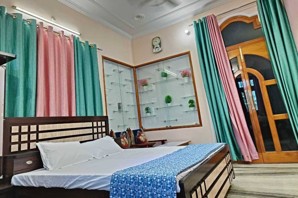 A bedroom with a bed, a nightstand, a mirror, a window with curtains, and a door.