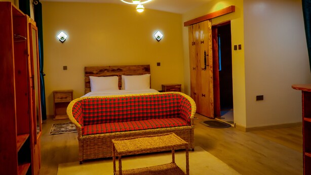 Une pièce comprenant un lit, un canapé à carreaux rouges et verts, une chaise en osier et une armoire en bois.