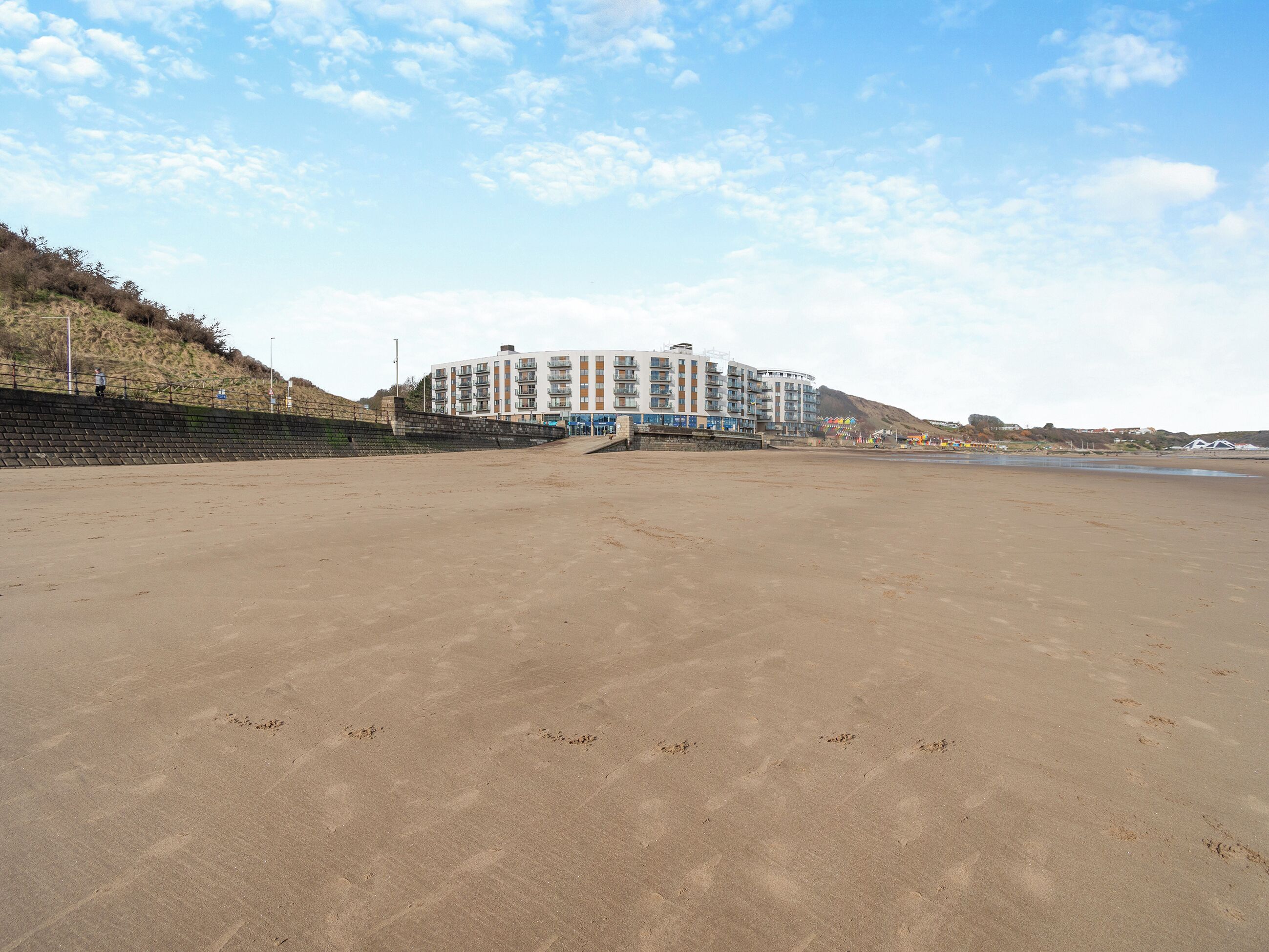 A beach with a large building in the background, a staircase leading up to it, and a clear sky.