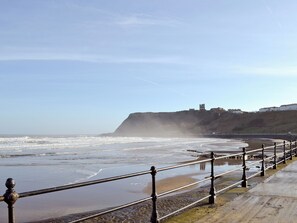 A coastal promenade with a metal railing, a cliff with a tower, and buildings in the background.