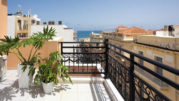 A balcony with potted plants, a view of the sea, and buildings in the background.