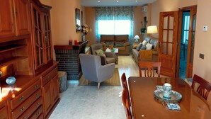 Een ruime woonkamer met een open haard, een eethoek met een houten tafel, en een keuken met houten kastjes.
