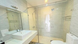 Een moderne badkamer met een douche met glazen wand, een wit wastafelmeubel en een toilet.