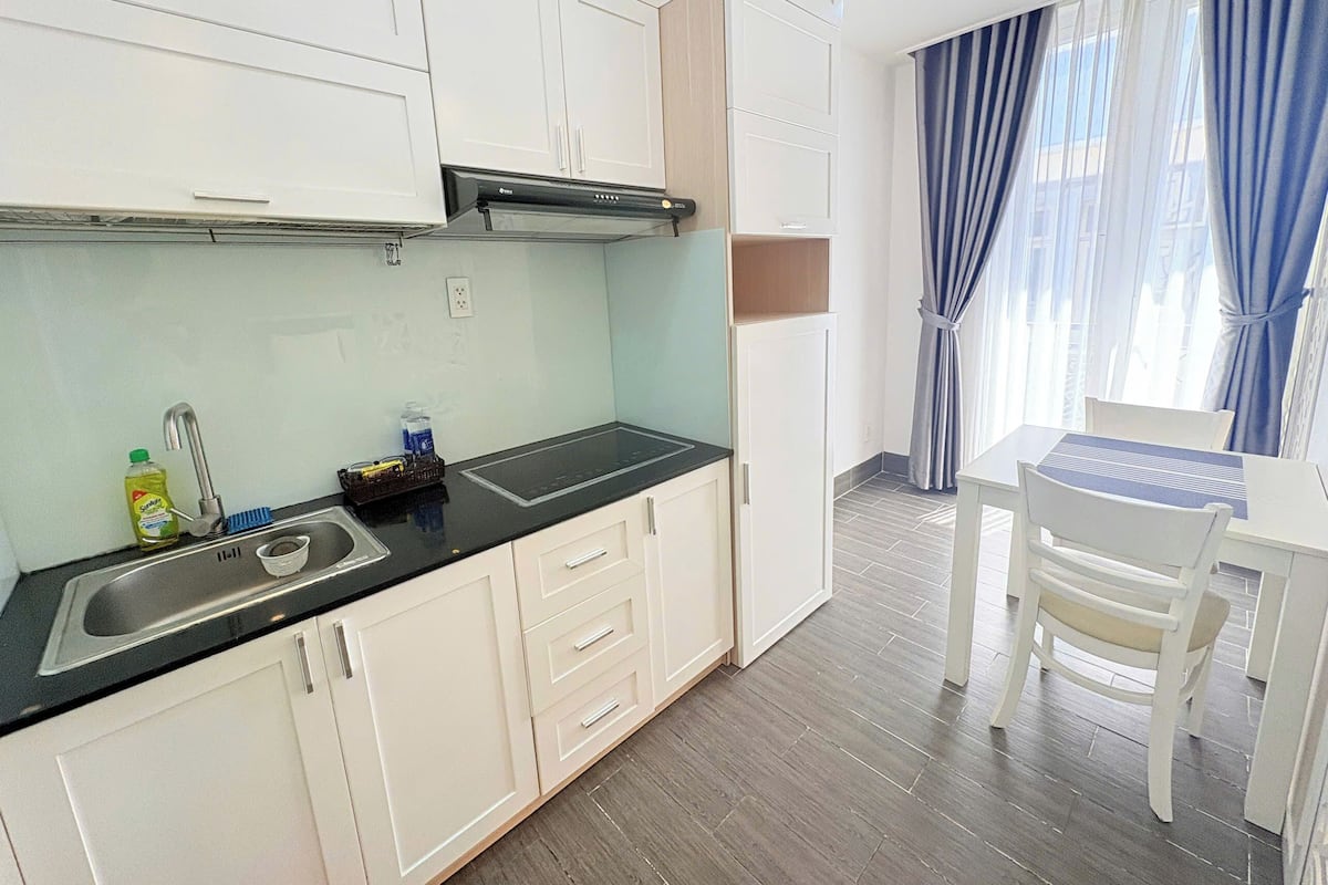 Een moderne keuken met witte kastjes, een zwart aanrecht en een spoelbak. Er is een eethoek met een tafel en stoelen.